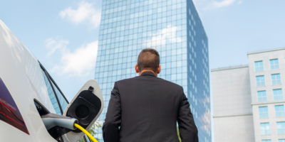 Homme devant un immeuble de bureaux avec une voiture électrique